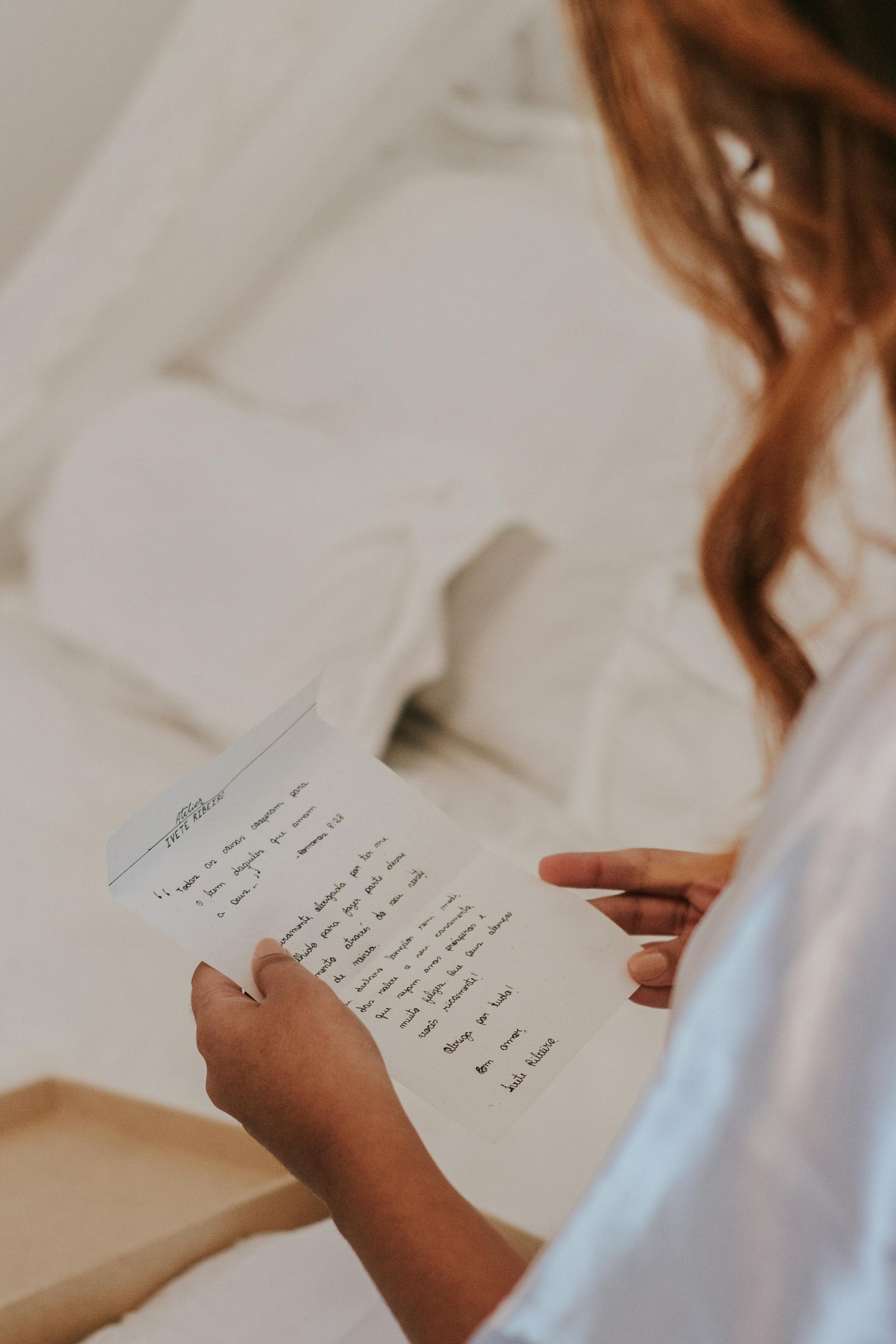 Close-up of a woman holding and reading a handwritten letter in a cozy bedroom setting.