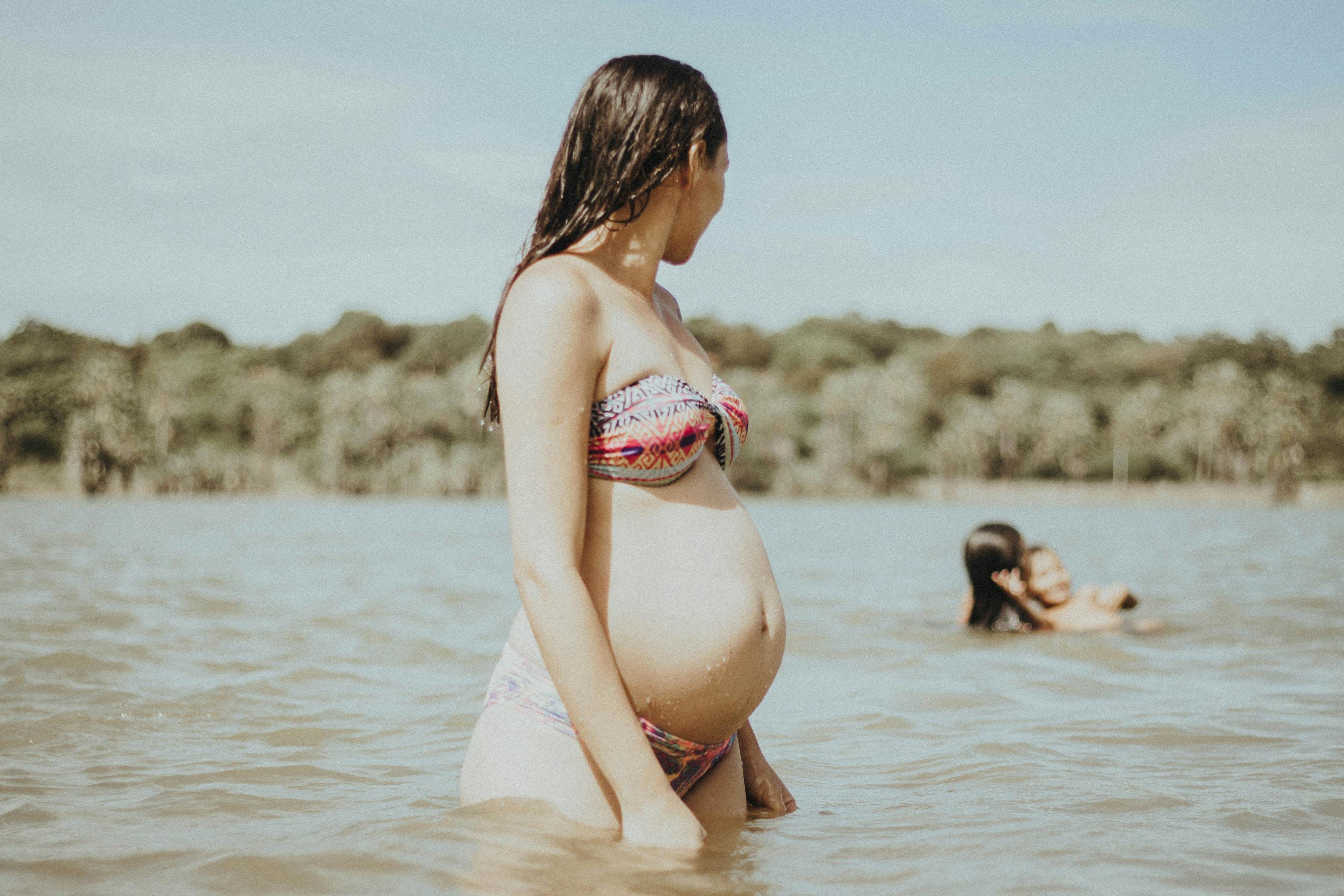 A pregnant woman in a colorful bikini standing in a river, enjoying the sunny day in Morrinhos, Brazil.