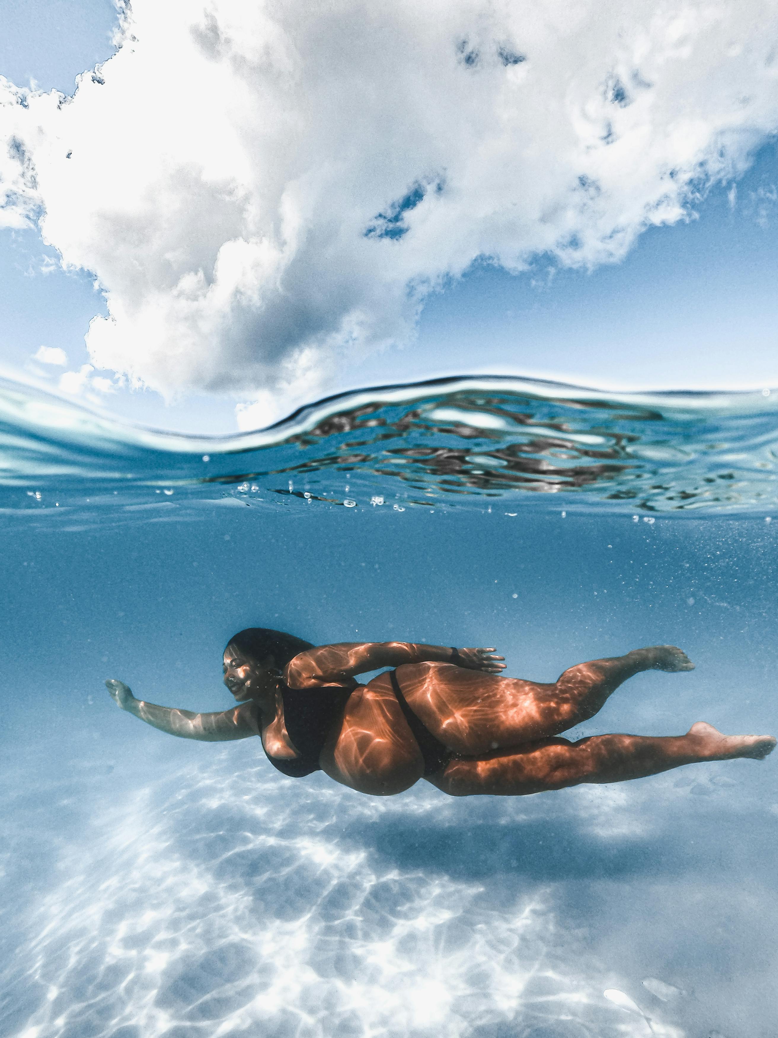 A serene image of a pregnant woman swimming underwater with sunlight reflections, showing strength and tranquility.