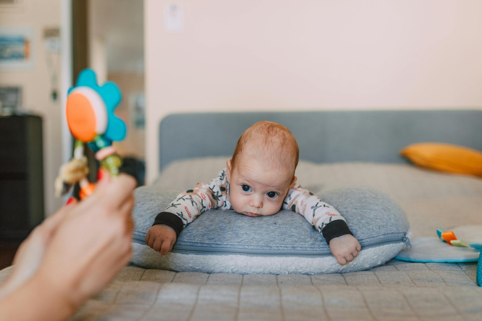 Cute baby on bed gazing at colorful toy, evoking warmth and curiosity.