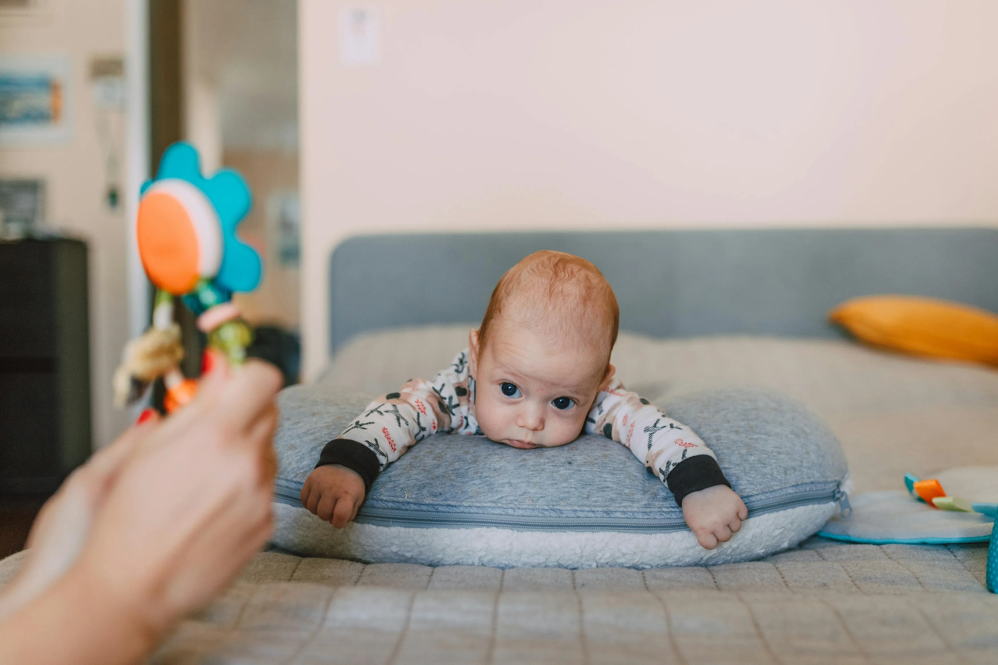 Cute baby on bed gazing at colorful toy, evoking warmth and curiosity.