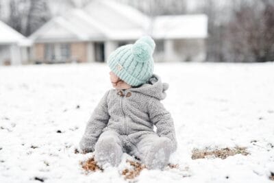 child in gray jacket and green knit cap sitting on snow covered ground during daytime