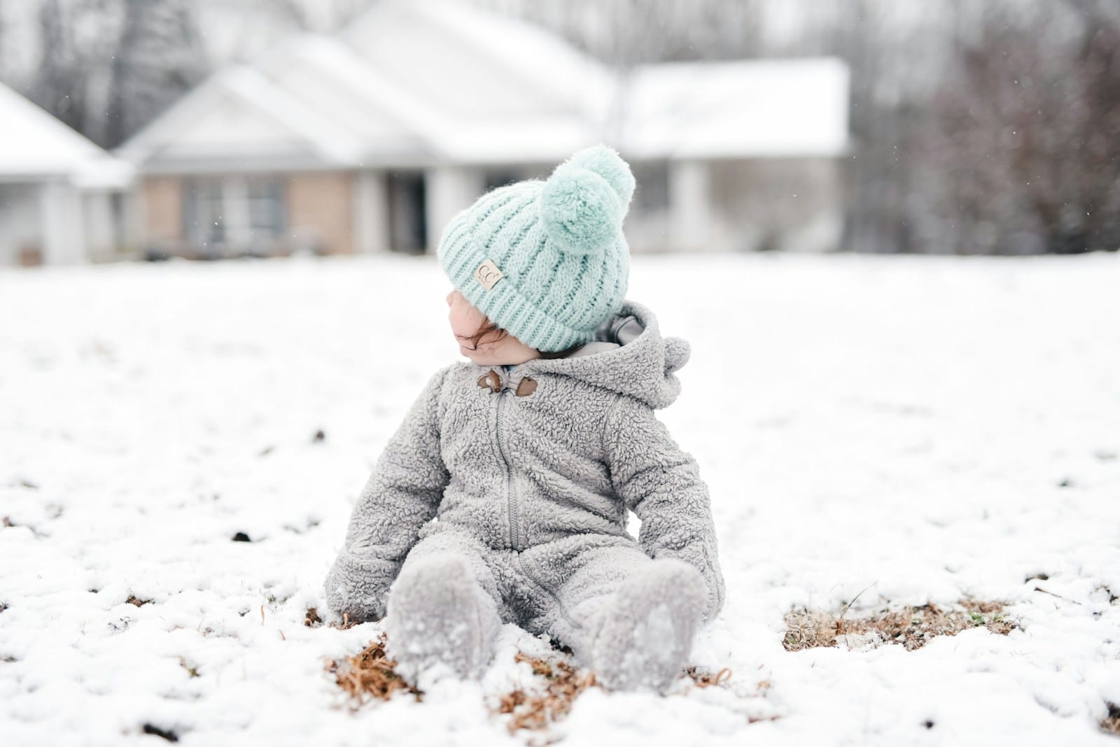 child in gray jacket and green knit cap sitting on snow covered ground during daytime