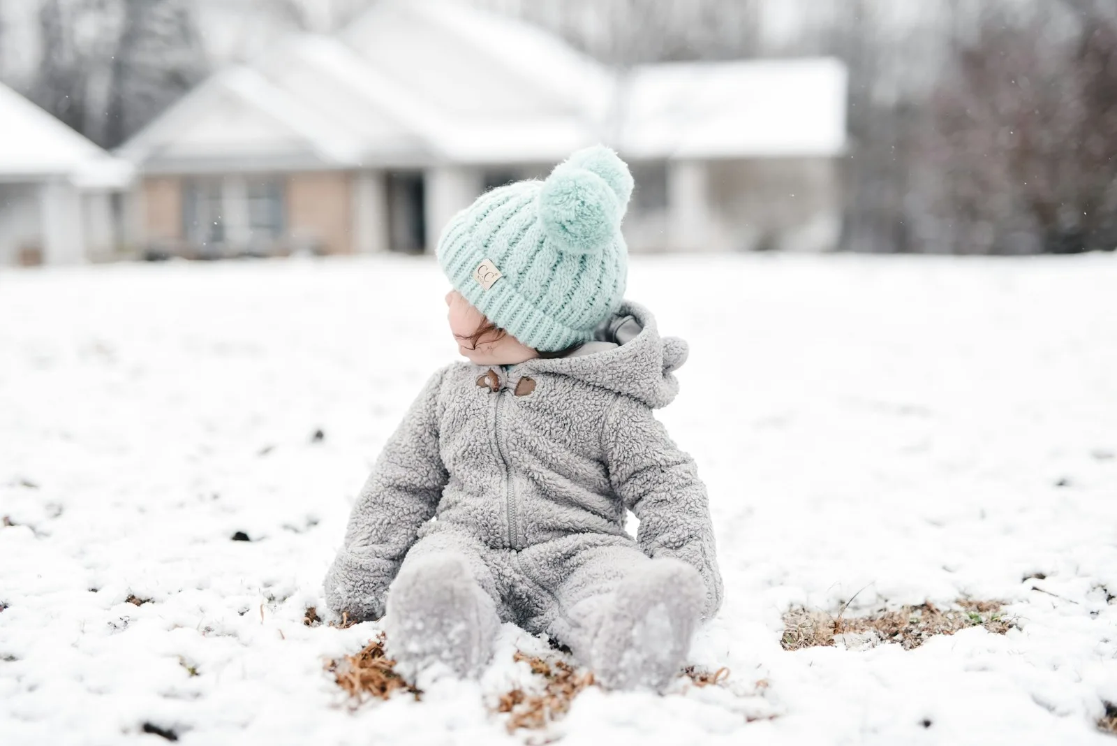 child in gray jacket and green knit cap sitting on snow covered ground during daytime